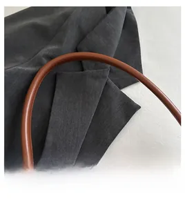 Detail of brown leather strap and dark grey suit fabric on a trendy baguette bag