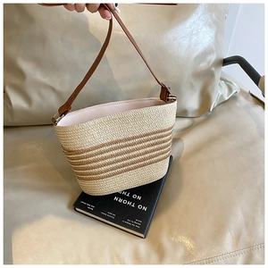 Close-up of woven straw bucket bag with brown stripes and leather shoulder strap detail