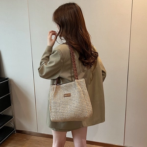 Sac fourre-tout en paille à poignées marron porté par un mannequin en costume vert