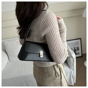 Close-up of a black leather-look baguette bag featuring a sleek golden turn-lock clasp