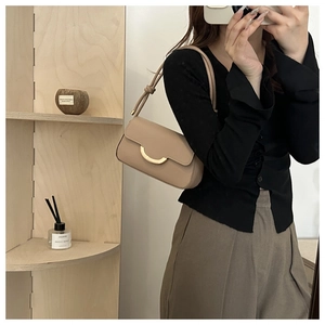 Detail of minimalist beige leather underarm bag with a polished gold semi-circle buckle