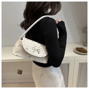 Detail of cream woven baguette bag with floral embroidery and golden bow buckle