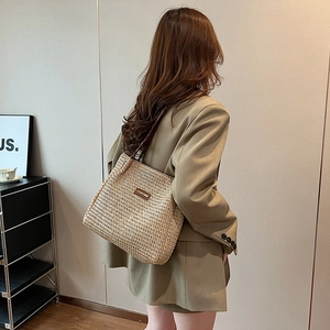 Détail d'un sac cabas en paille tissée avec patch logo en cuir et anses en corde tressée