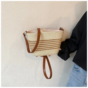 Detail of woven straw bucket bag with brown leather strap and contrast stripes