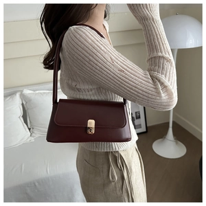 Detail of a deep red baguette shoulder bag with a gold metal clasp in a modern interior