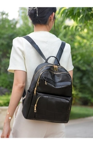 Outdoor view of a black quilted leather backpack with three zipper compartments and gold hardware