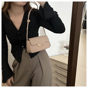 Detail of light beige leather baguette bag featuring a gold half-moon clasp and knotted strap