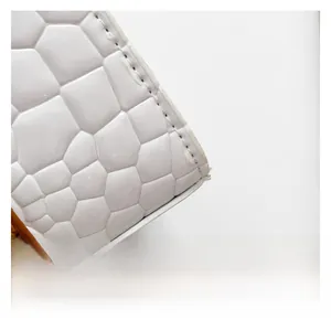 Primer plano del bolso de piel blanca con relieve de cocodrilo, ribete marrón y costura