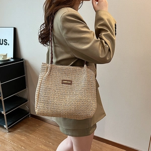 Fashionable striped woven tote bag with brown leather tag shown on shoulder with blazer