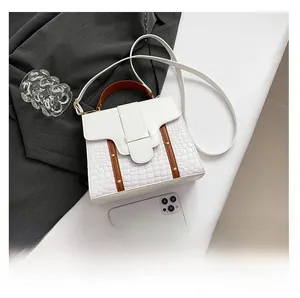 Detalle de bolso blanco con grabado de cocodrilo, asas marrones y remaches dorados
