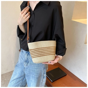 Detail of woven straw crossbody bag with dark brown stripes and slim leather strap