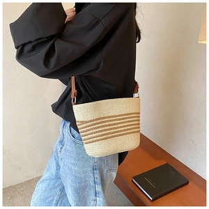 Straw crossbody bag with brown leather strap worn by a model in a minimalist setting