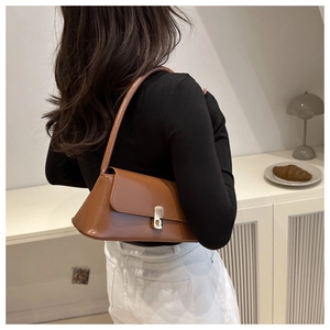 Detailed view of a brown leather baguette bag with a silver buckle worn on the shoulder