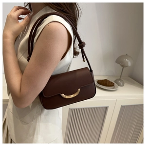 Detail of dark brown leather bag showing gold buckle and decorative knot shoulder strap