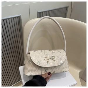 Detail of cream woven shoulder bag with floral embroidery and golden bow hardware