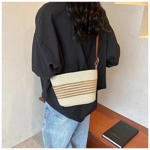 Detail of a woven straw crossbody bag with brown stripes and leather strap on a model