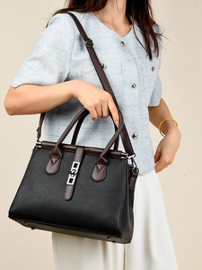 Classic black leather tote bag with brown handles and silver clasp shown on a model