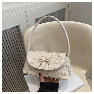 Detail of beige straw baguette bag with floral embroidery and golden bow clasp