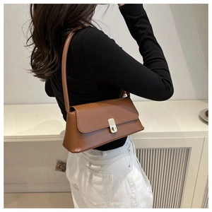 Detail of vintage brown leather baguette bag with golden buckle on female shoulder