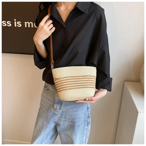 Detail of handwoven straw bucket bag with brown stripes and slim leather shoulder strap