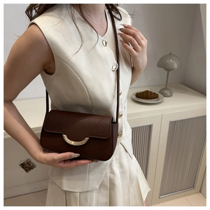 Brown vintage leather shoulder bag with gold crescent buckle on a beige outfit