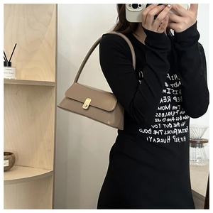 Detailed view of taupe minimalist baguette bag with gold metal clasp on a wooden shelf