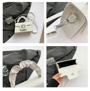 Detail of white crocodile embossed mini handbag featuring rhinestone buckle and bear charm