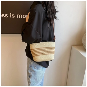Detail of hand-woven straw bucket bag with brown stripes and leather shoulder strap