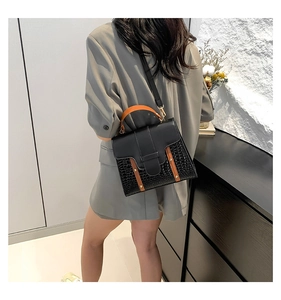 Detalle de bolso bandolera de piel sintética negra con textura de cocodrilo y tiras naranja