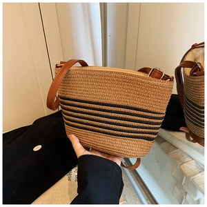 Close-up of woven straw bag with black stripes and adjustable brown leather strap
