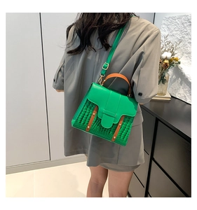 Detail of green crossbody bag with crocodile texture, orange strap and rivet accents