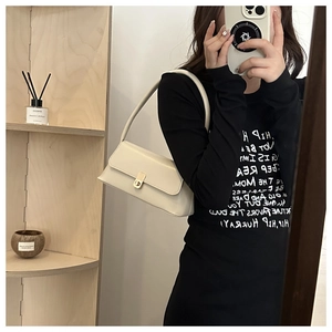 Detail of a creamy white baguette bag with a bright gold buckle on a model's shoulder