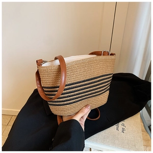 Detail of woven straw bag showing natural texture, black stripes, and brown leather straps