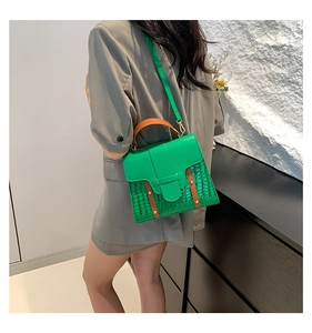 Detail of green faux crocodile leather crossbody bag with contrasting orange handle