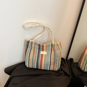 Détail d'un cabas en paille à rayures colorées avec logo en cuir et bandoulière tressée
