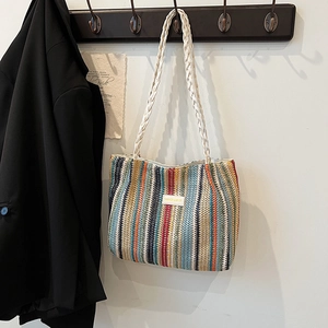 Détail du sac cabas tissé à rayures colorées avec poignées tressées sur un crochet mural