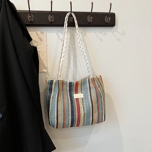 Détail d'un cabas rayé en paille tissée avec des anses en corde blanche et un patch cuir