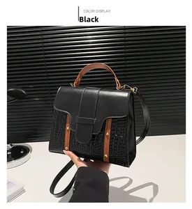 Detail view of black textured leather handbag with brown handles and gold hardware
