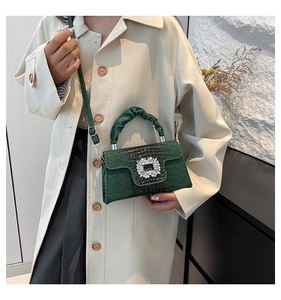 Detail of emerald green crocodile pattern handbag with crystal buckle and ruched handle