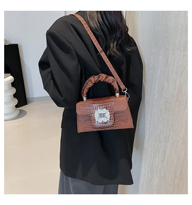 Brown crocodile embossed handbag with rhinestone buckle worn as a crossbody bag