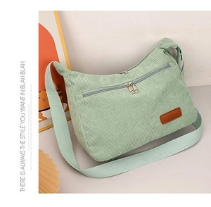 Detail of mint green corduroy crossbody bag featuring a front pocket and wide shoulder strap