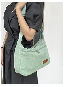 Detail of light green corduroy crossbody bag with adjustable strap and fashion label
