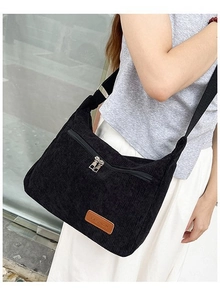 Close-up of black corduroy crossbody bag with metal zipper and leather fashion label