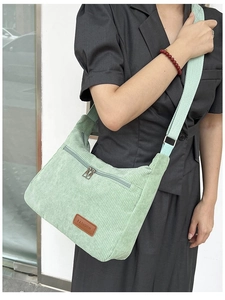 Close-up of light green corduroy crossbody bag featuring a FASHION label and front zipper