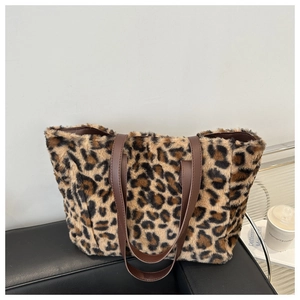 Leopard print plush tote bag with brown leather straps displayed on a black surface