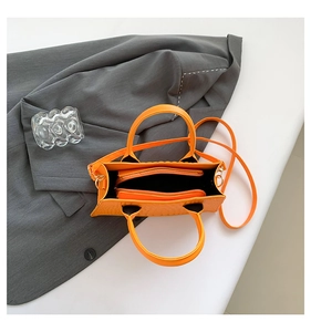 Detail view of bright orange crocodile pattern handbag with interior zip compartment