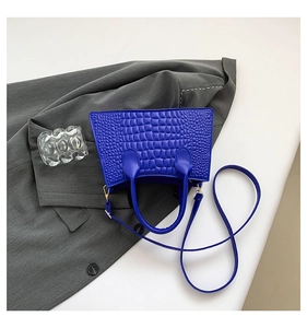 Detail of blue crocodile pattern PU leather handbag with gold hardware on grey suit