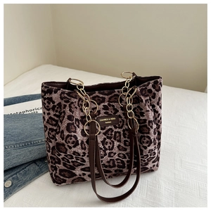 Detail of leopard print tote bag with brown leather handles and gold chain ornament