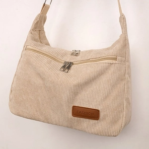 Detail of beige corduroy crossbody bag featuring dual front zippers and a leather brand tag