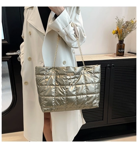 Detail of gold quilted tote bag with metallic sheen, chain strap and deer pendant on model